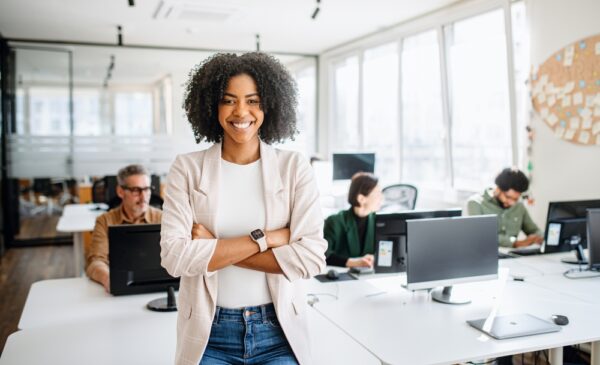 A woman with folded arms and a big smile stands proud at a workplace that is using healthy habits.